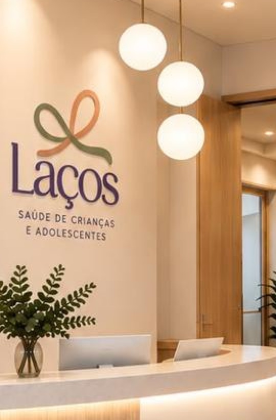 Recepção da Laços, com balcão iluminado, pendentes de vidro e a marca na parede